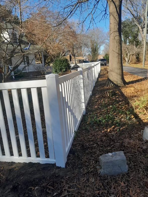 a white fence is sitting next to a tree in a yard