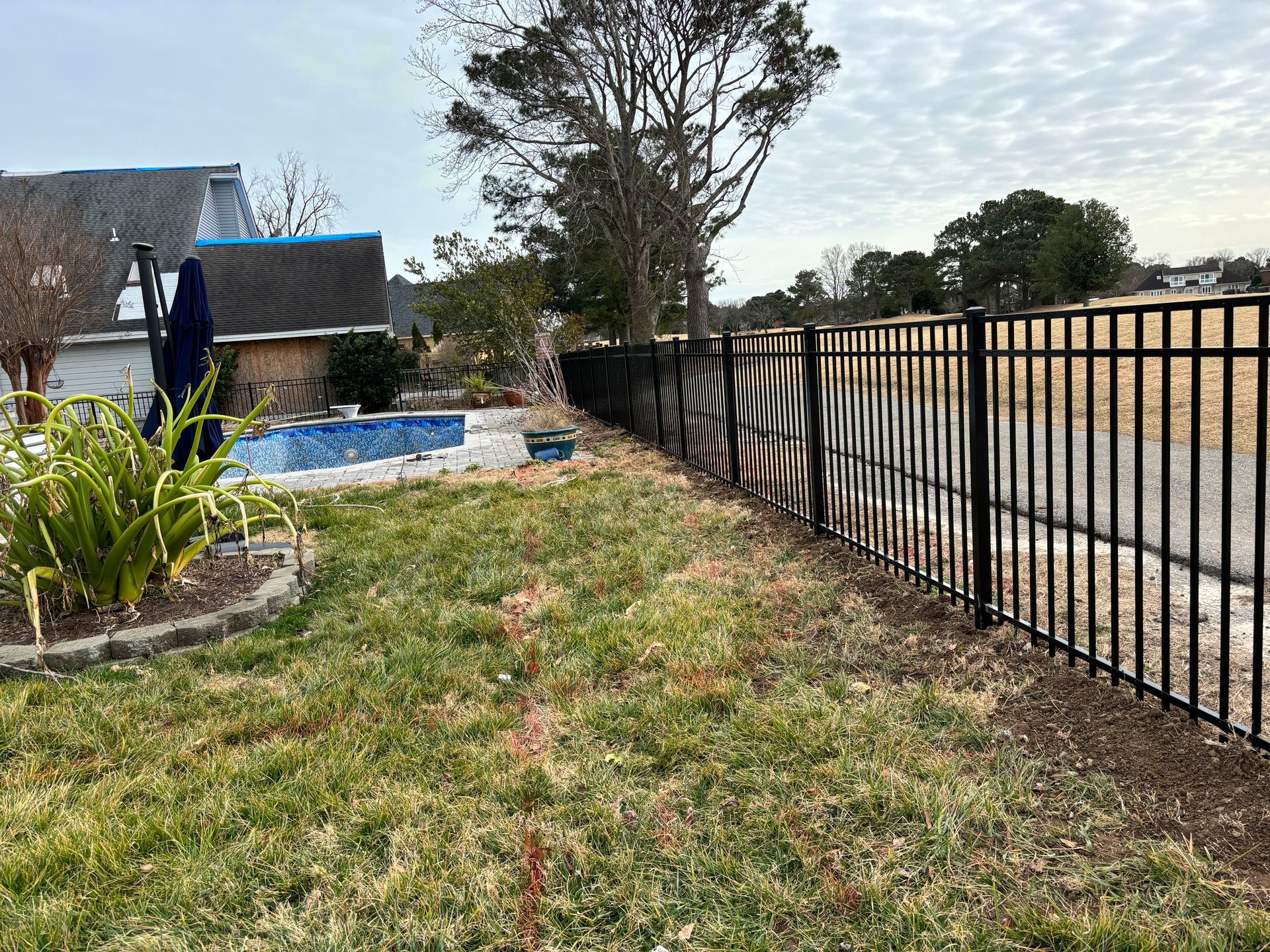 a black fence surrounds a backyard with a pool and a house in the background