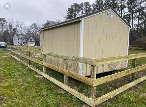 a shed behind a wooden fence in a grassy field
