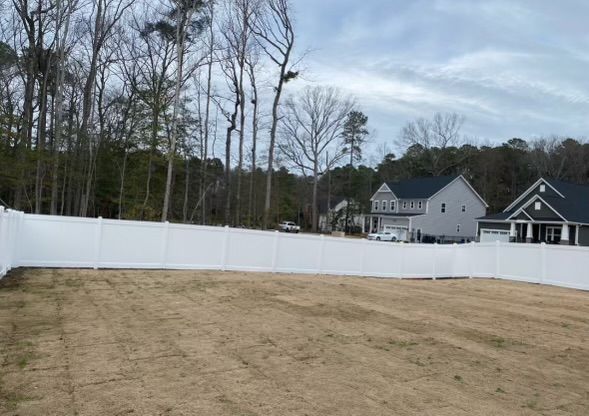 a white fence surrounds a large grassy field in front of a house