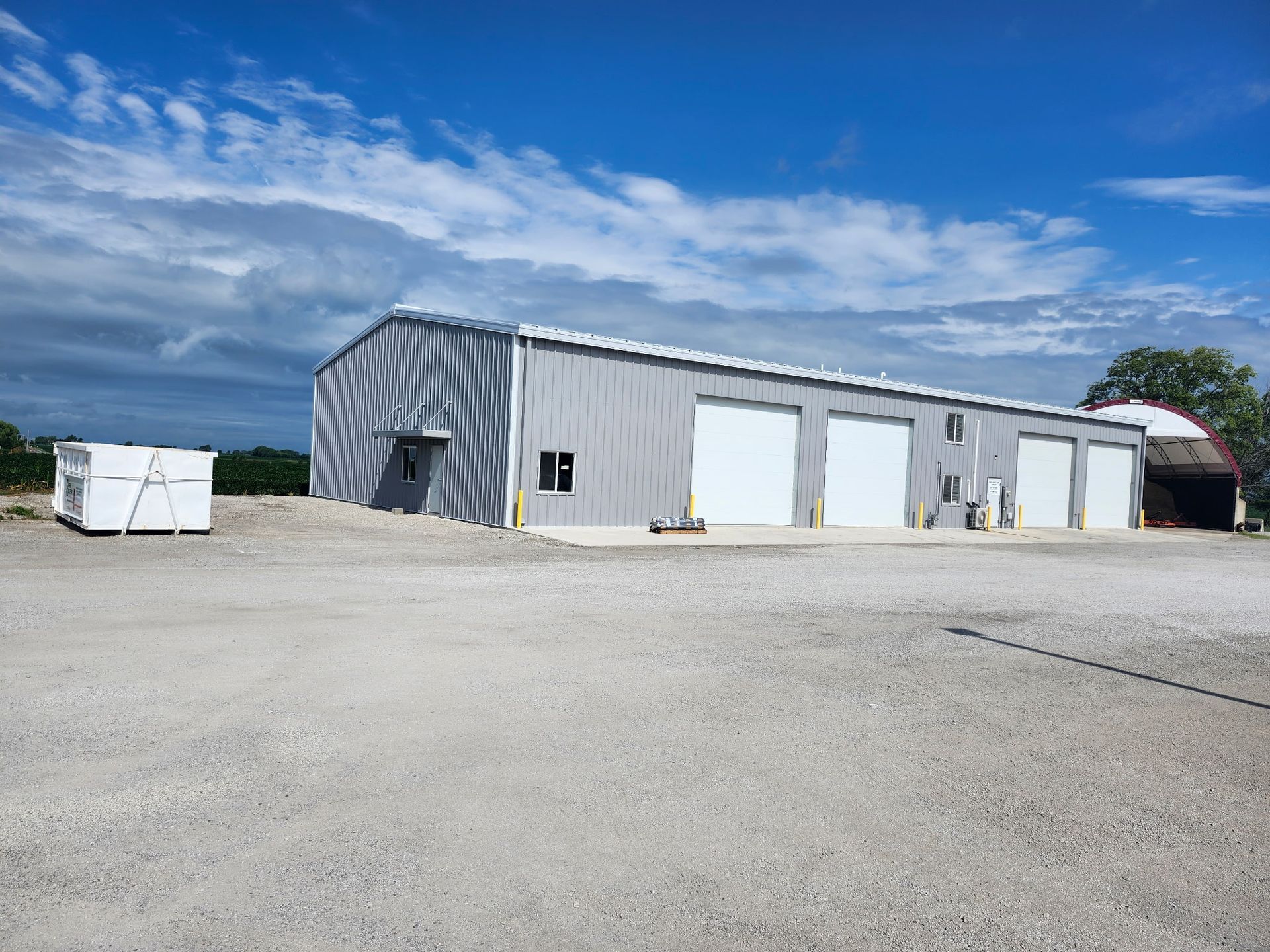 Gray metal building with three garage doors, gravel lot, blue sky.
