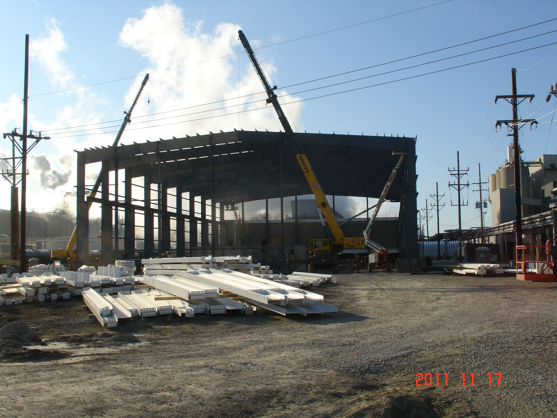 Construction site: steel building frame with two cranes, power lines, and materials.