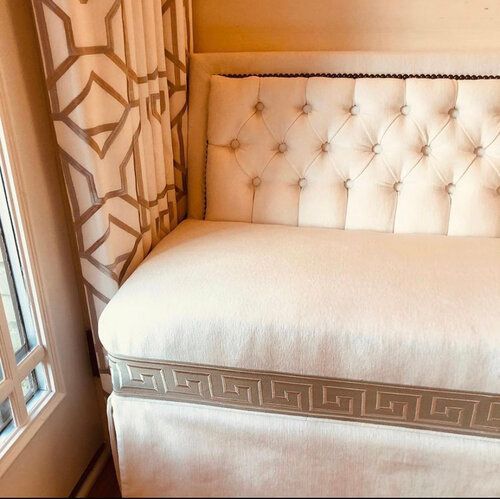 A white couch with a greek key trim sits next to a window