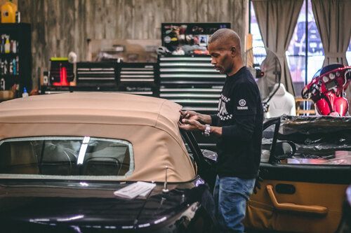 A man is working on a convertible car in a garage.