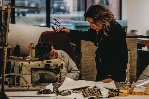 A woman is teaching a man how to use a sewing machine.