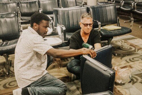 Two men are sitting in a waiting room looking at a laptop.