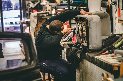 A man is sitting on a stool in a garage working on a chair.