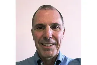 Smiling man in a blue shirt against a light pink background