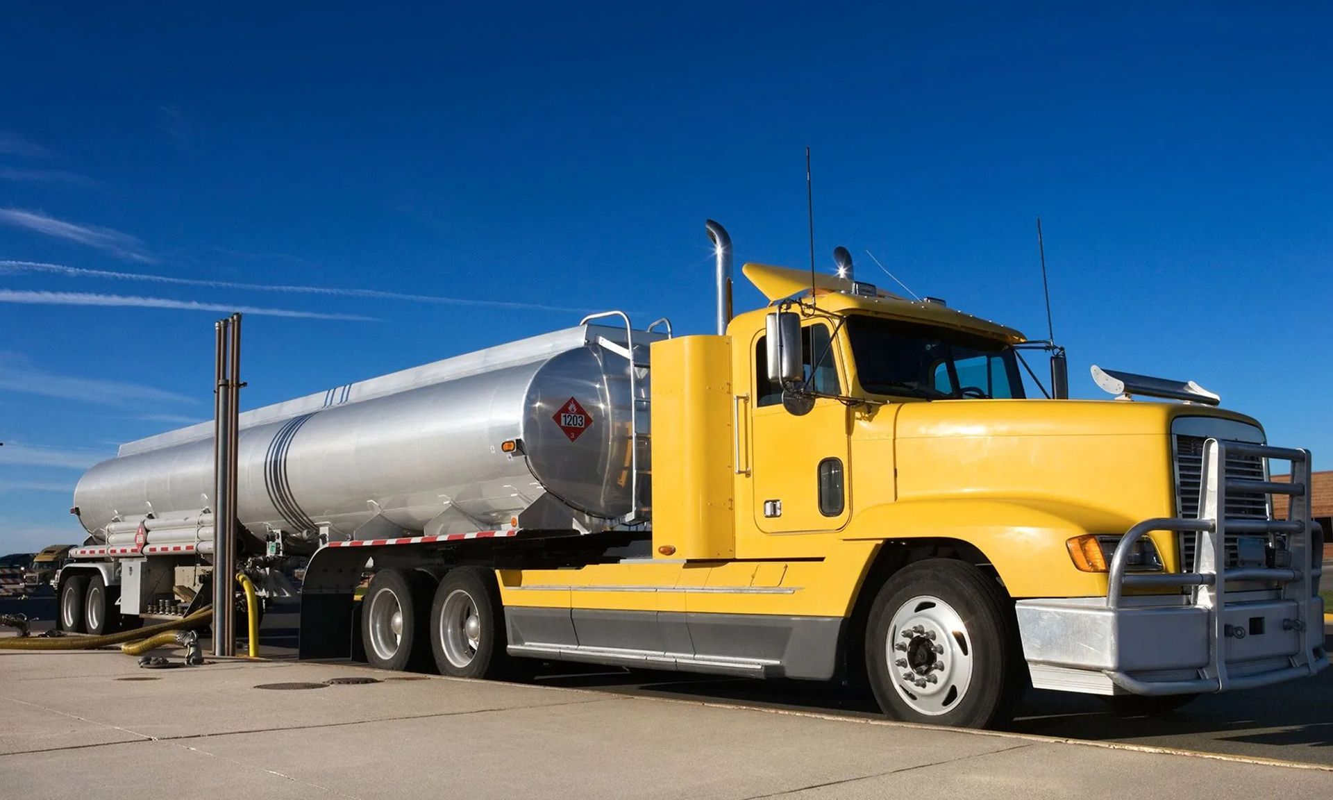Yellow tanker truck parked on pavement under a blue sky
