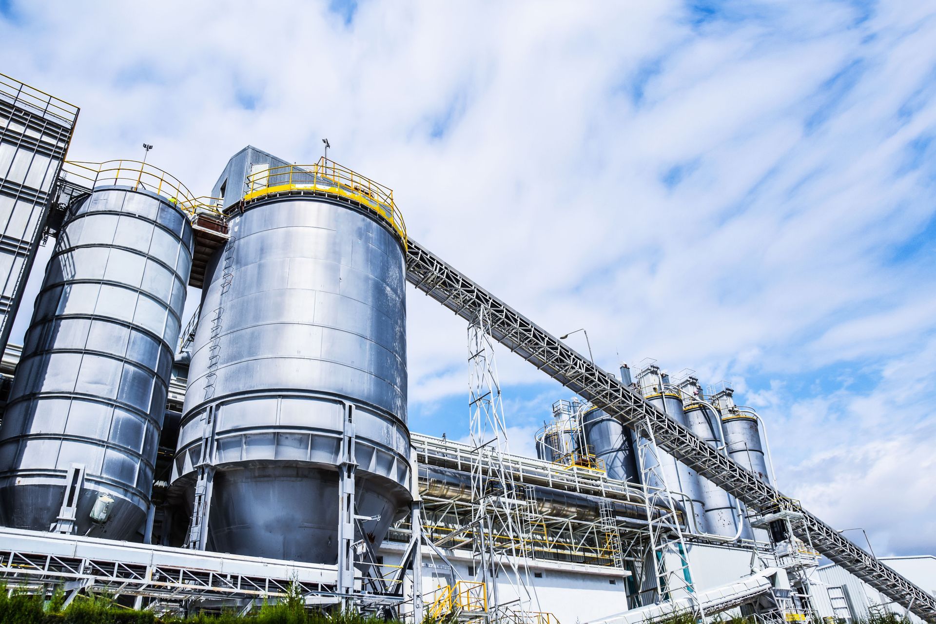 Industrial refinery with large silver storage tanks and pipes under a blue sky