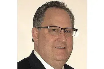 Portrait of a man wearing glasses and a dark suit against a light background