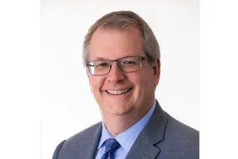 Smiling man in glasses wearing a gray suit and blue tie against a white background