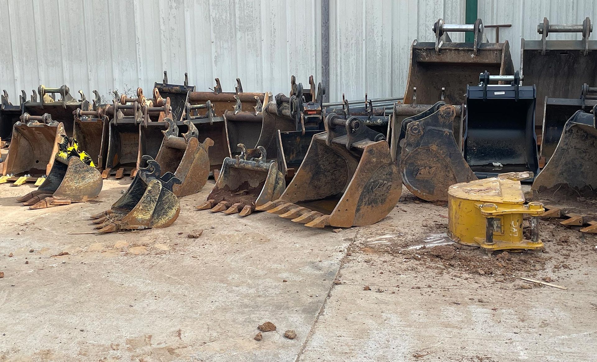 A row of excavator buckets are lined up on the ground