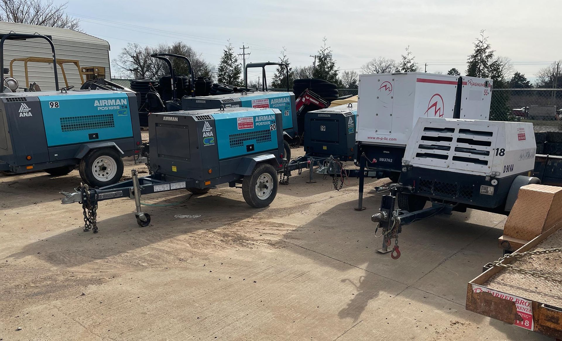 A row of trailers are parked in a dirt lot.