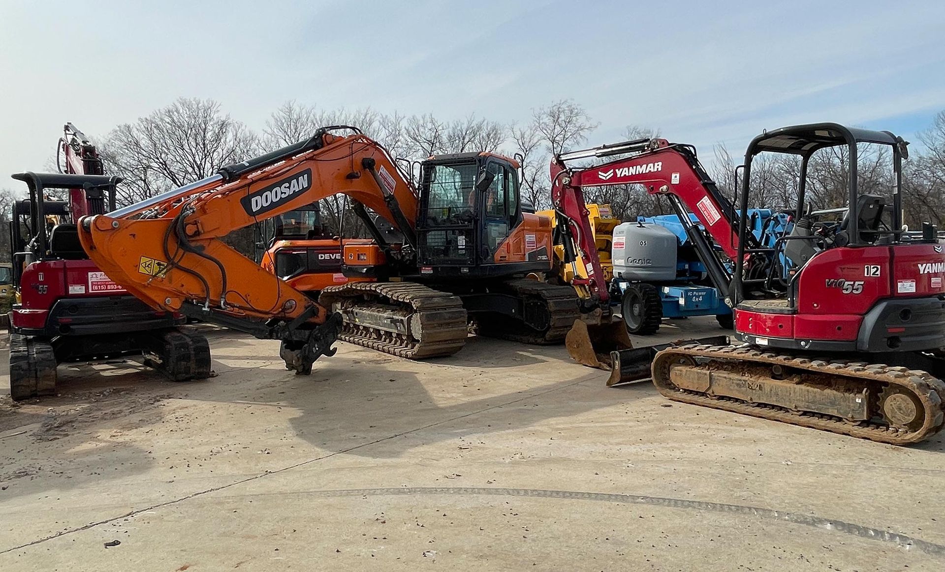 A group of construction vehicles are parked in a dirt lot.