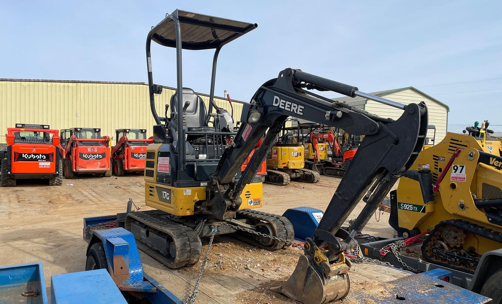 A small excavator is sitting on top of a trailer in a parking lot.