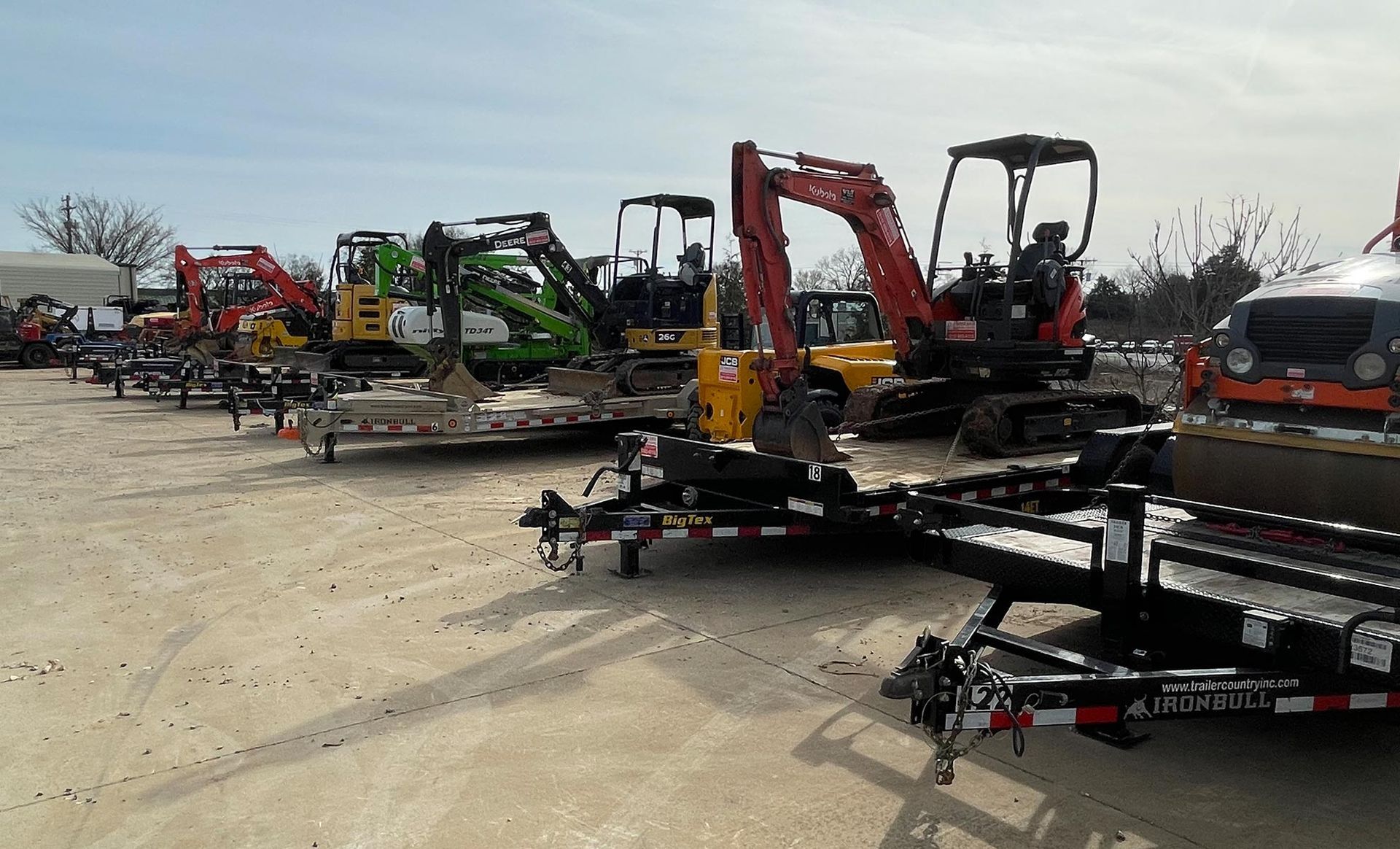 A row of construction vehicles are parked in a parking lot.