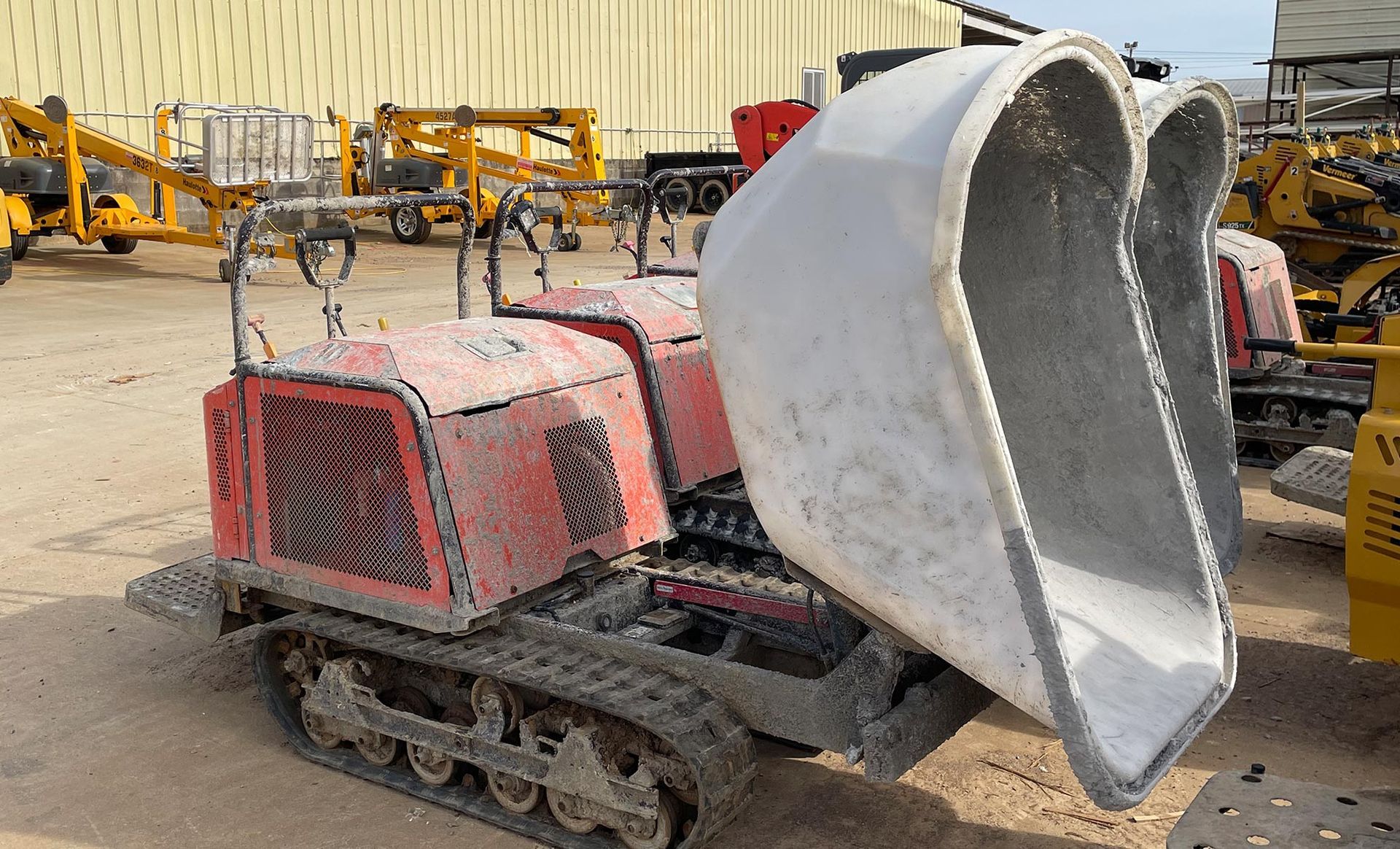 A red and white dump truck is parked in a dirt lot