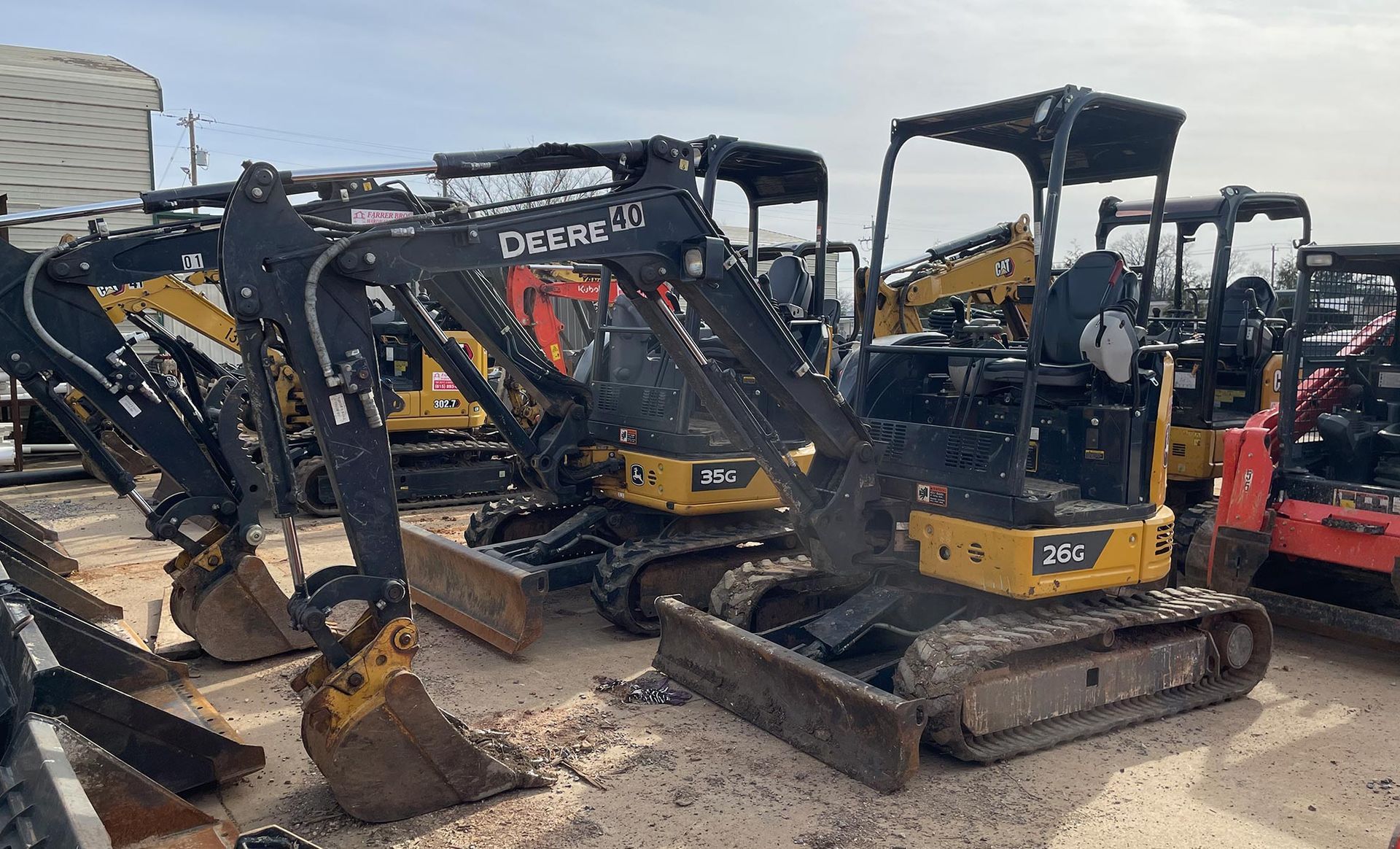 A row of excavators are parked in a lot.