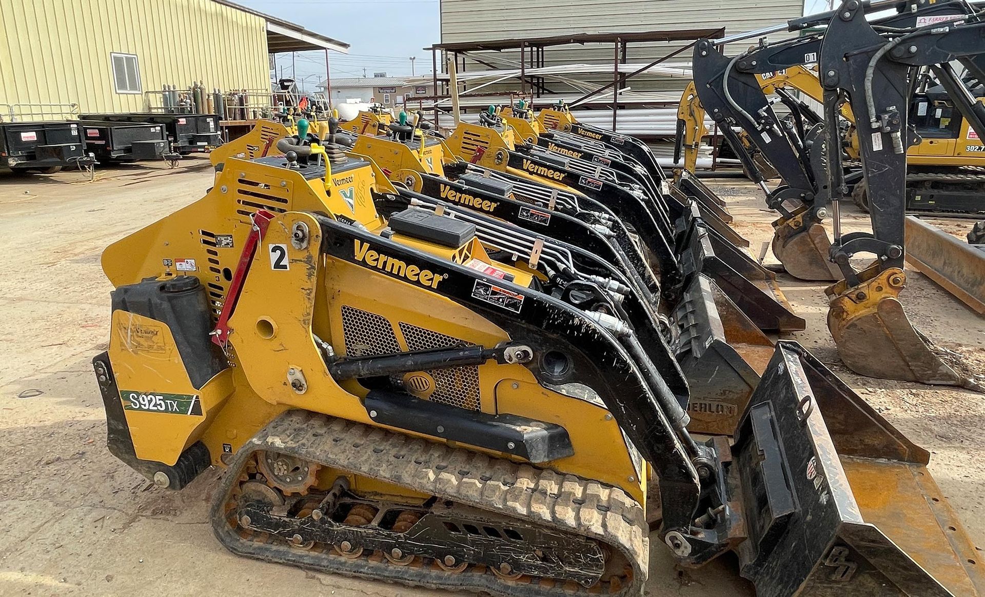 A row of yellow and black tractors are parked in a lot.