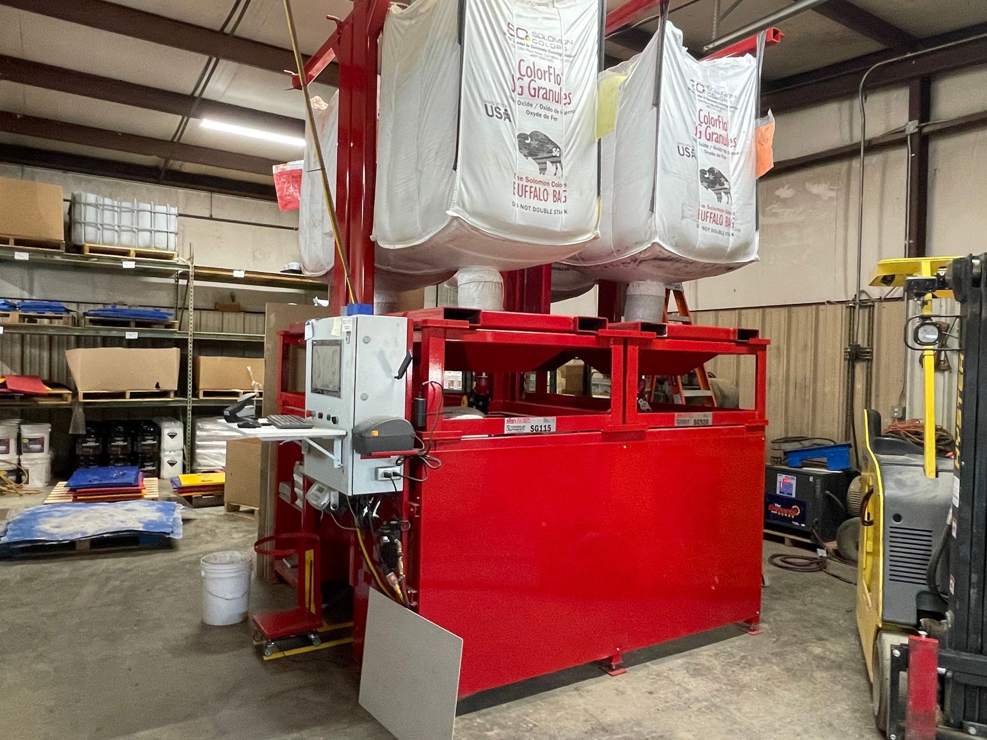A red machine is sitting in a warehouse next to a forklift.