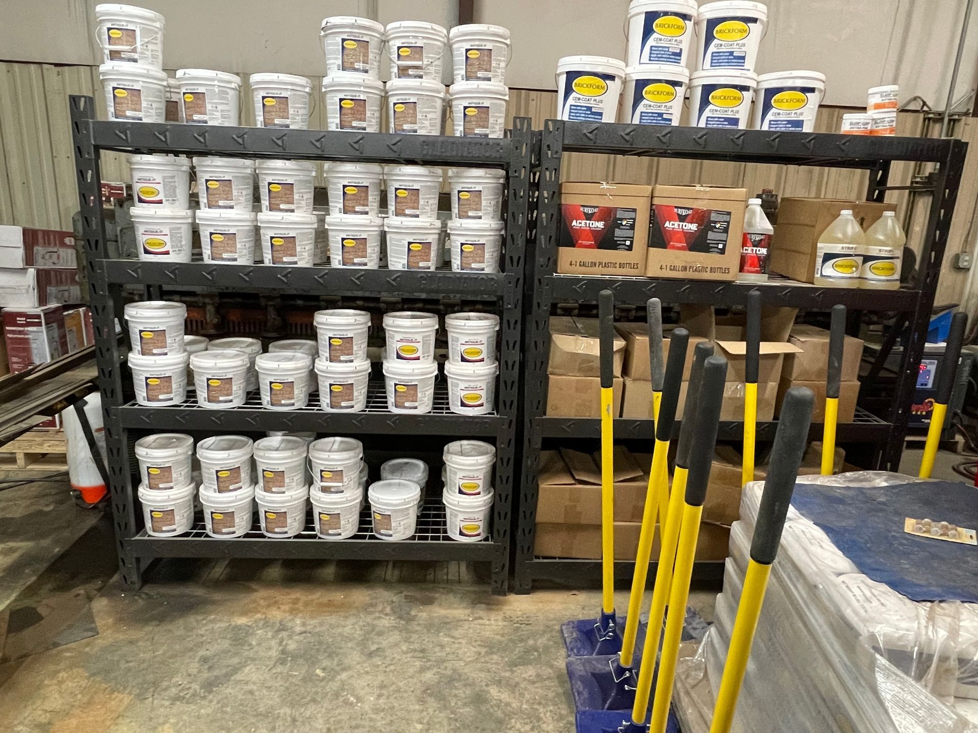 A warehouse filled with lots of buckets of paint and mop sticks.