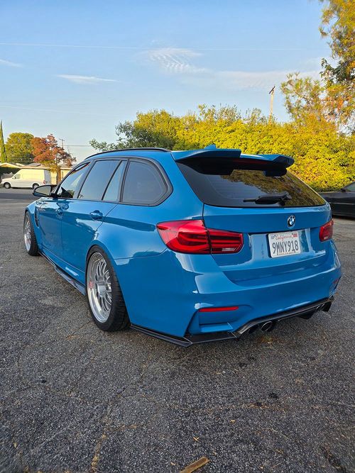 Blue BMW SUV parked on gravel lot under a clear sky, rear three-quarter view