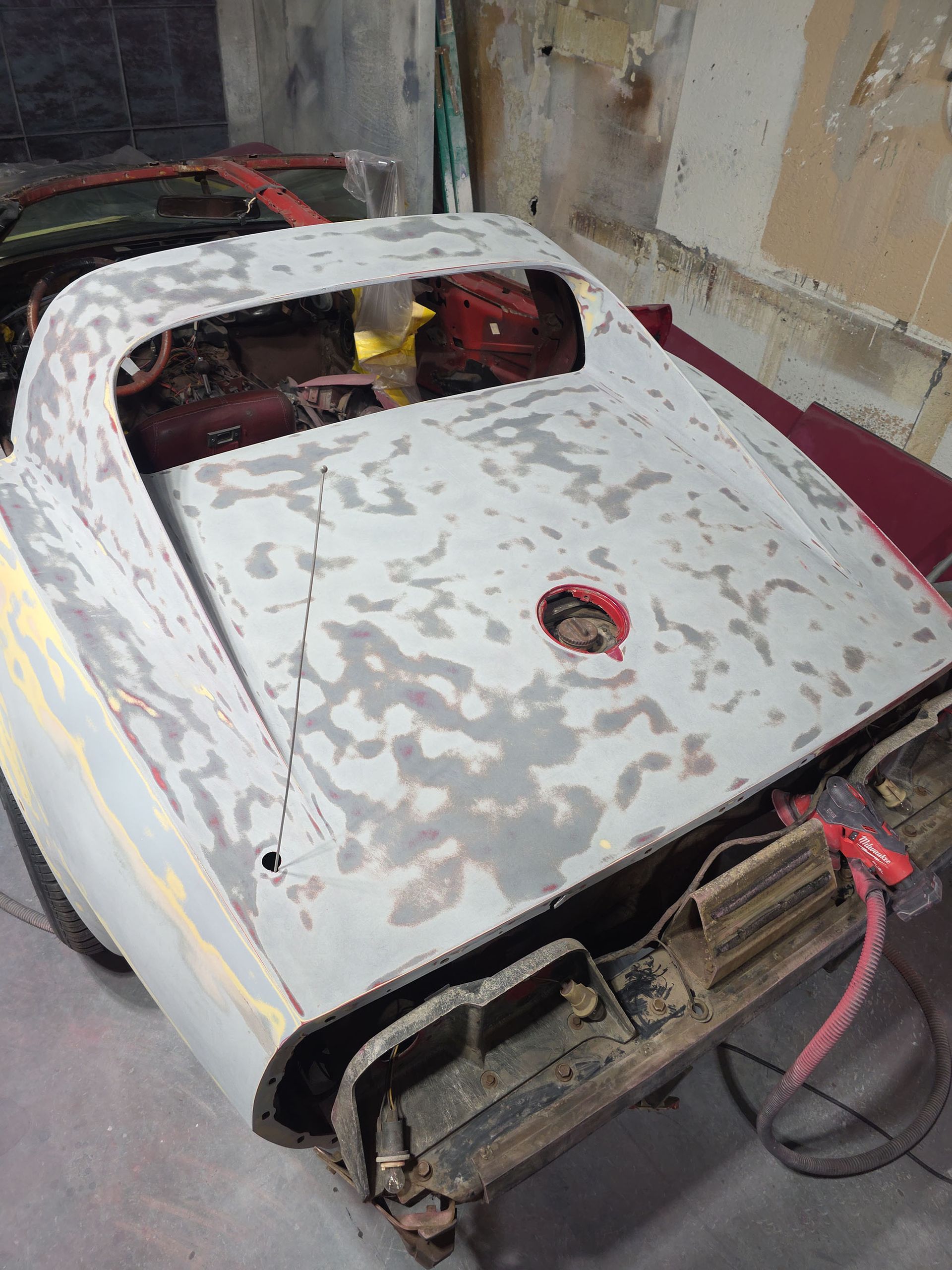 Weathered white metal panel on a red vehicle chassis in a workshop, with a circular opening and exposed wiring.