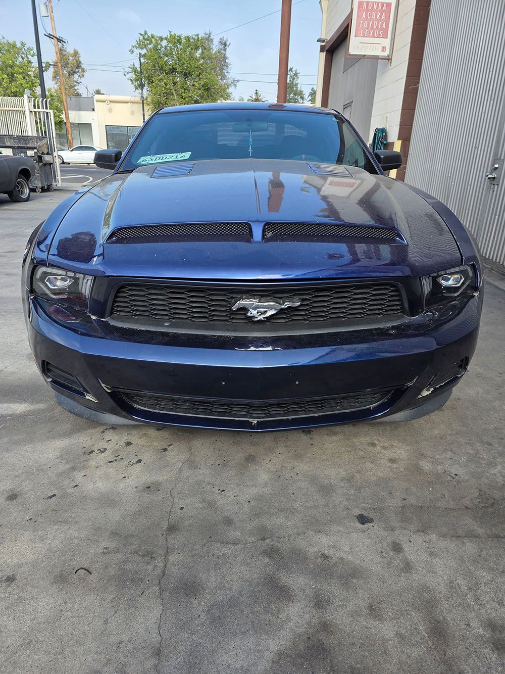 Front view of a dark blue Ford Mustang parked in a narrow alley.