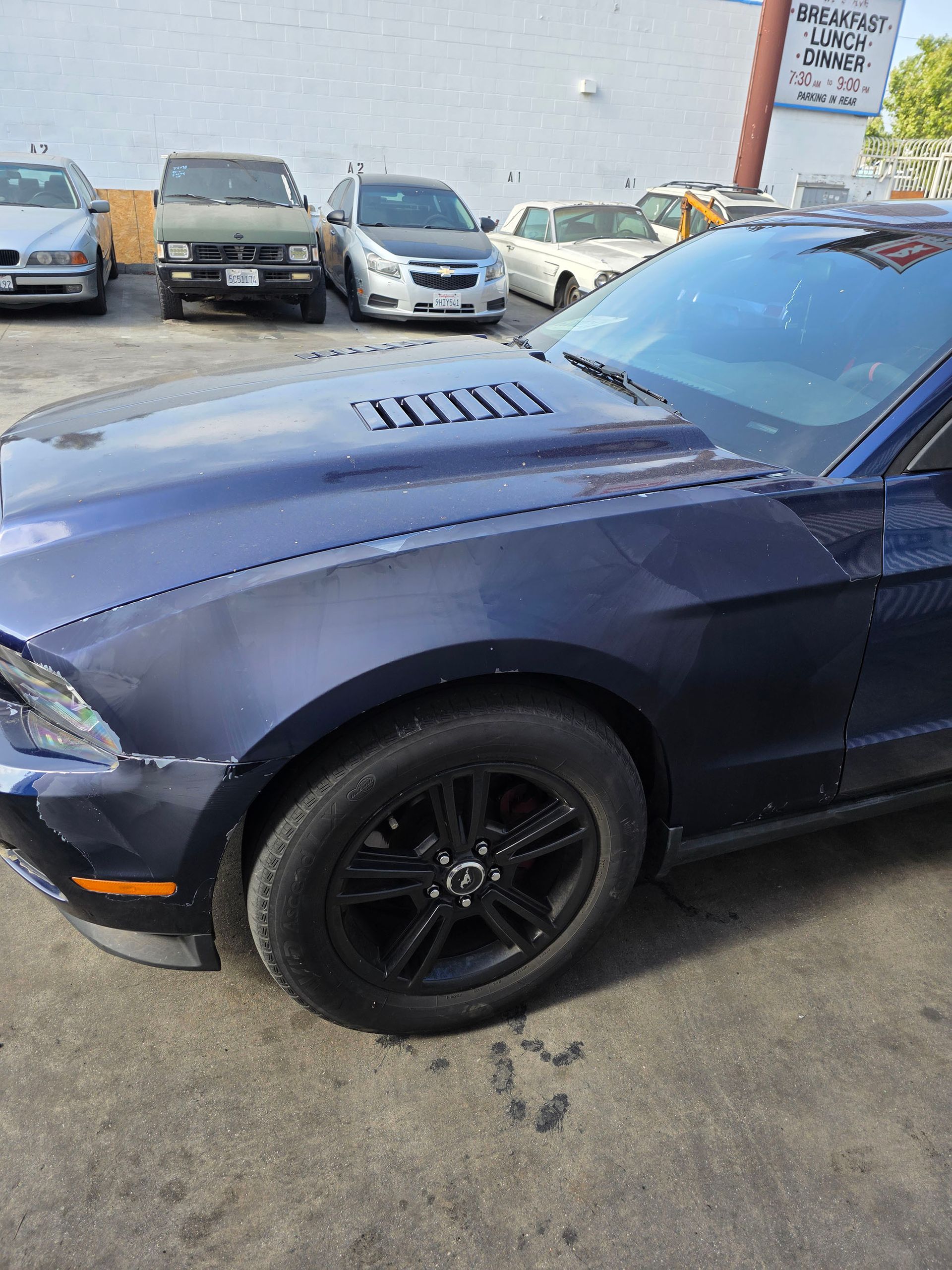 Dark blue sports car parked outdoors in a lot, with other cars in the background.