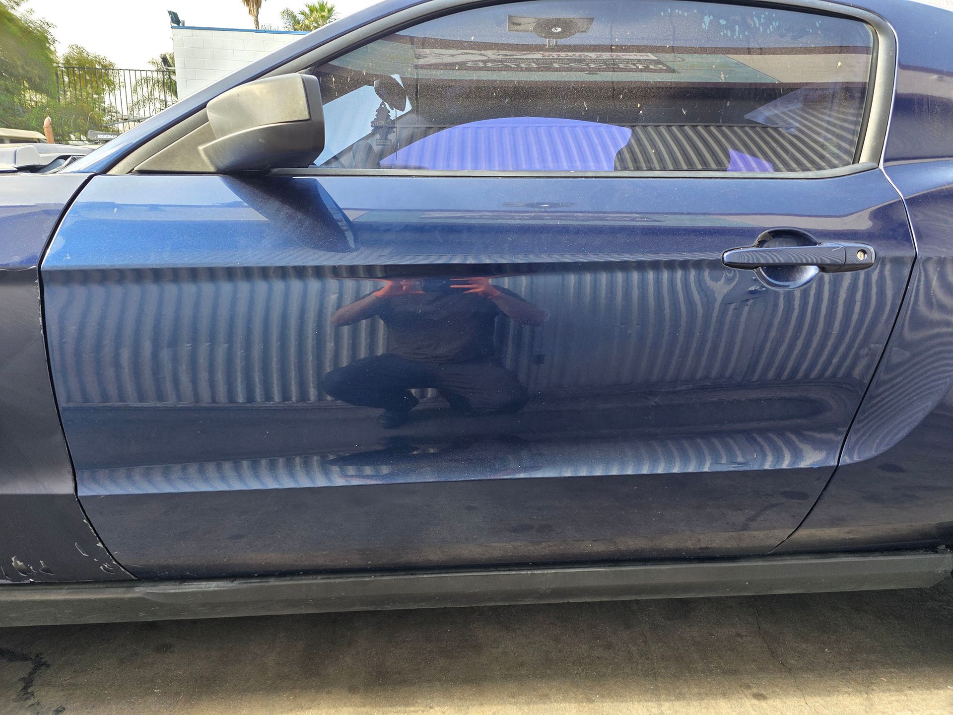 Blue convertible car door and side mirror, seen from the side on a paved surface.