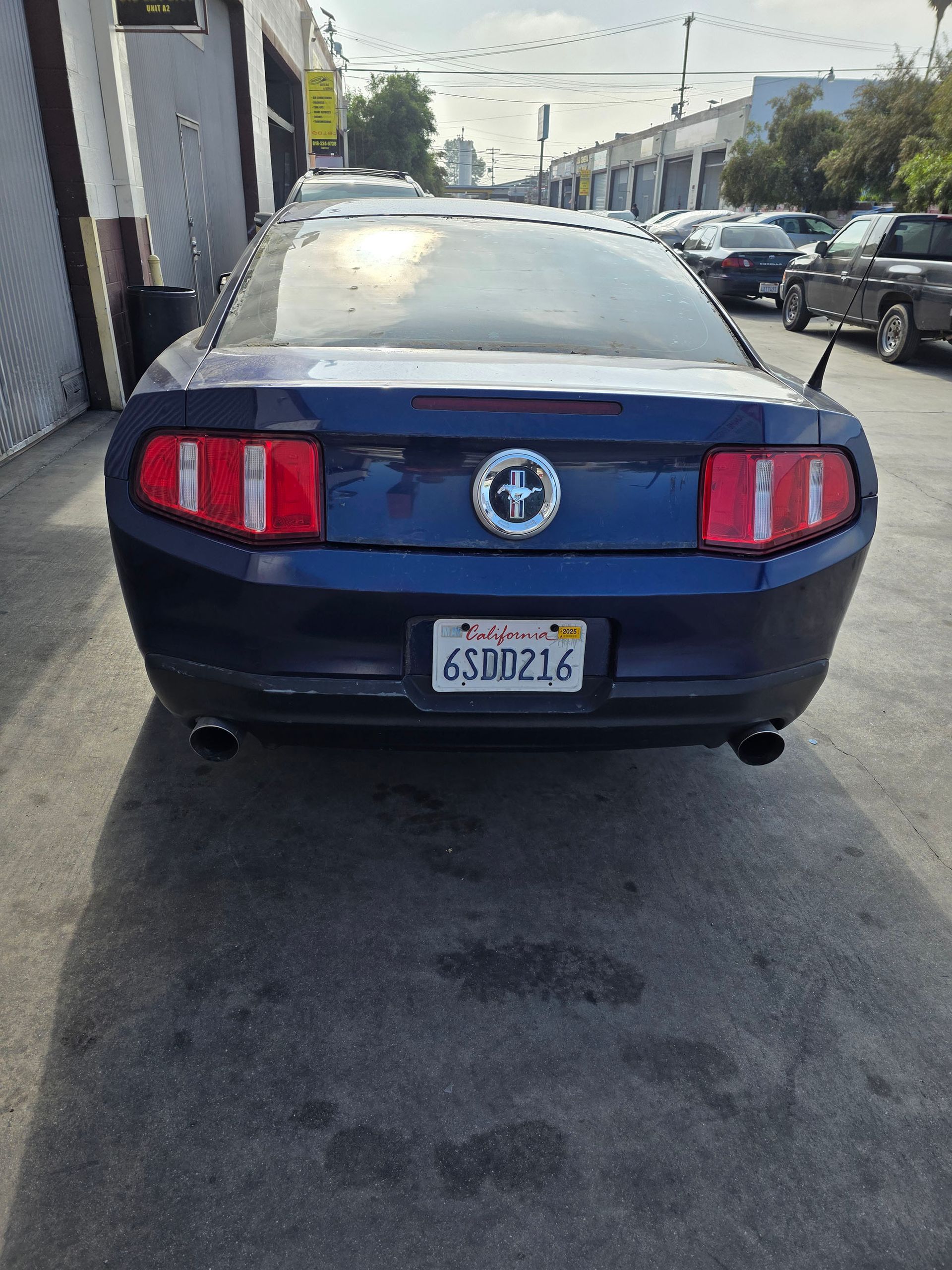 Rear view of a blue Ford Mustang parked on a street, with a white top and red taillights.