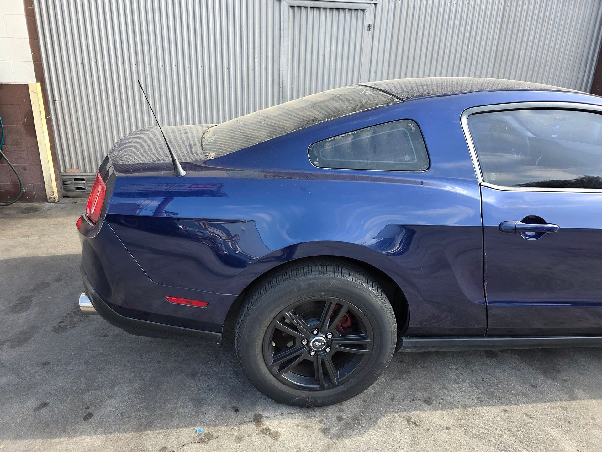 Blue sports coupe parked beside a corrugated metal wall, rear side view