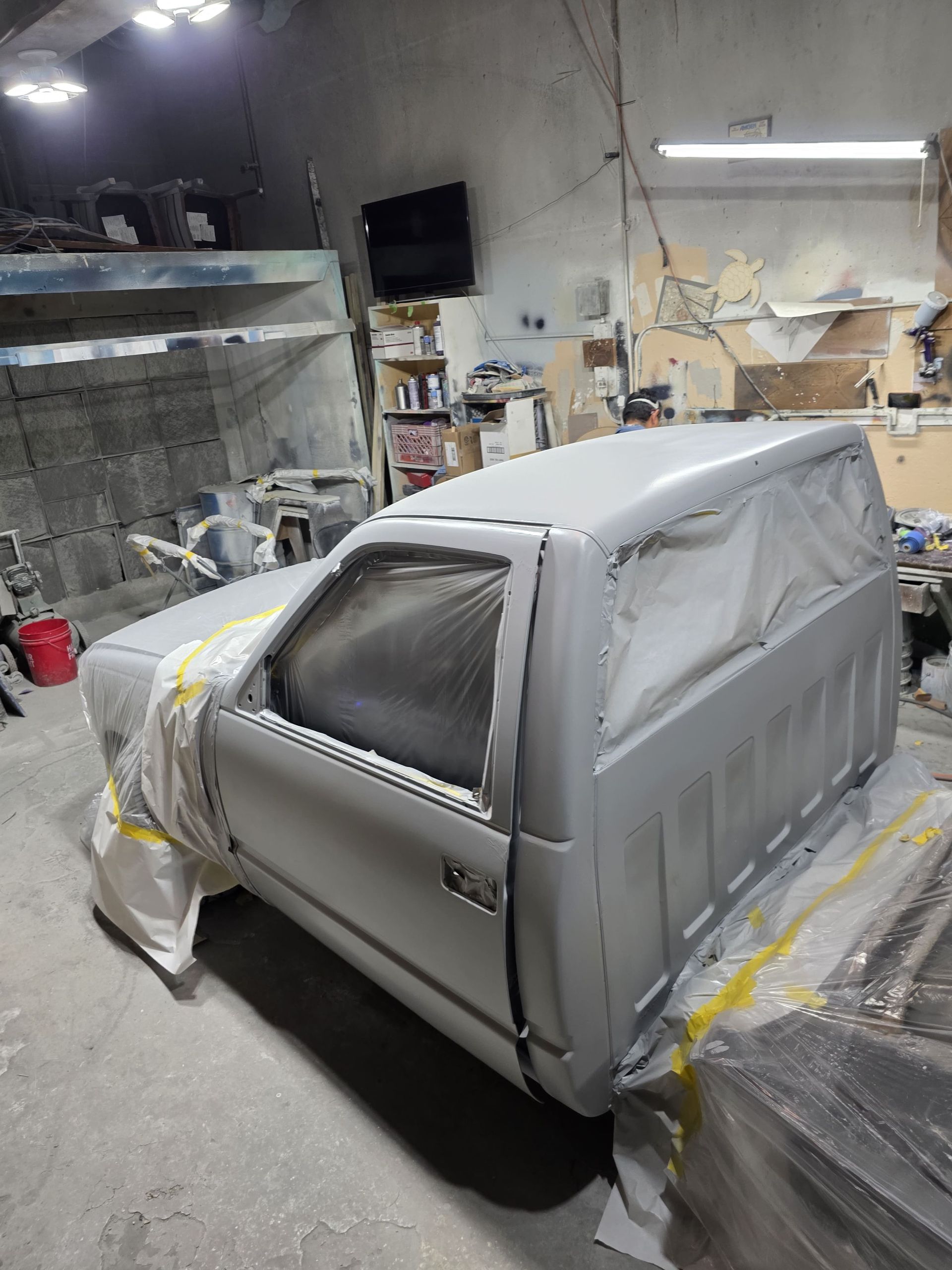 Car covered in protective masking and tape inside an auto paint shop