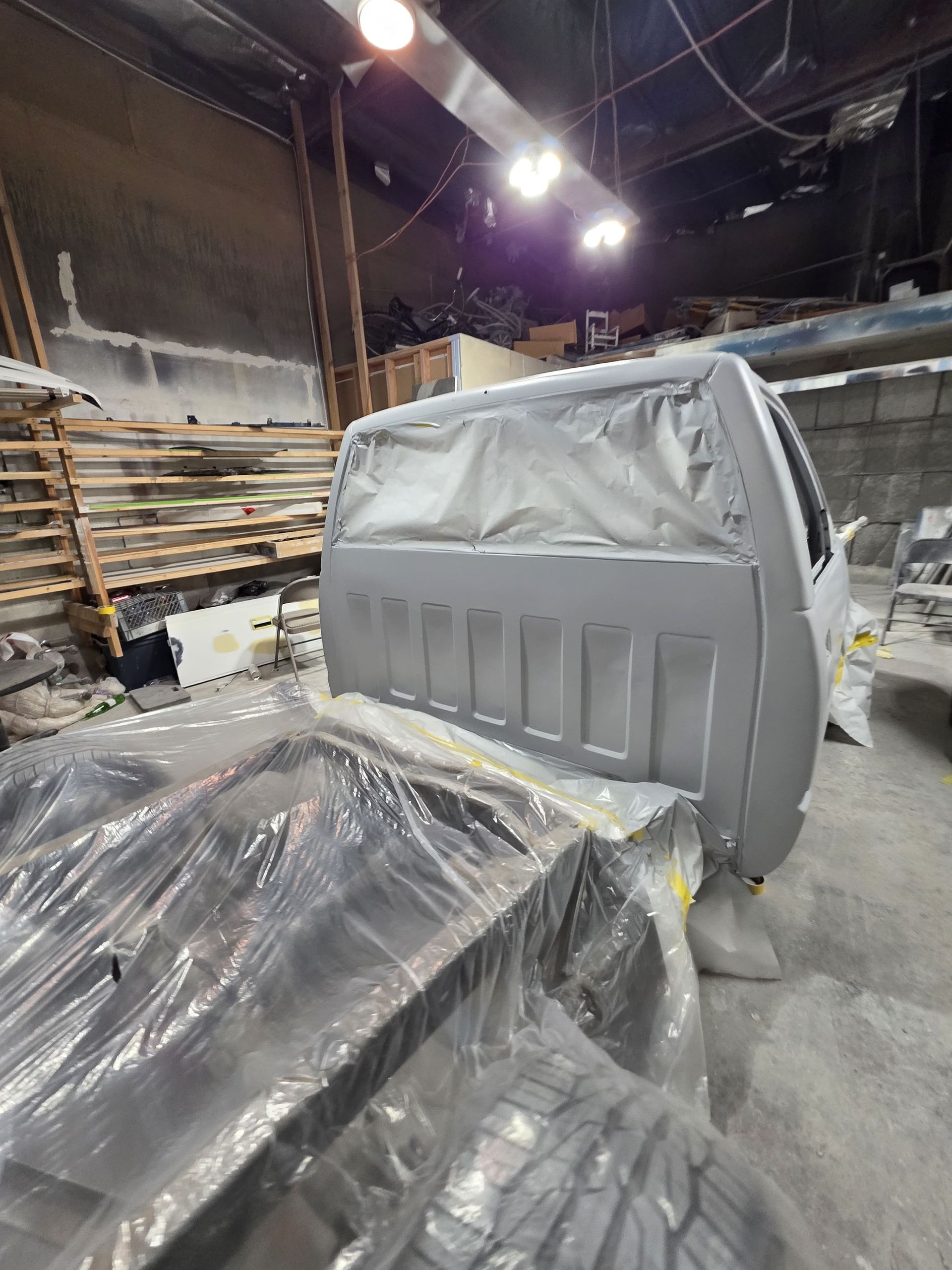 Masked truck cab and bed in an industrial warehouse, covered in plastic sheeting during painting or repair.