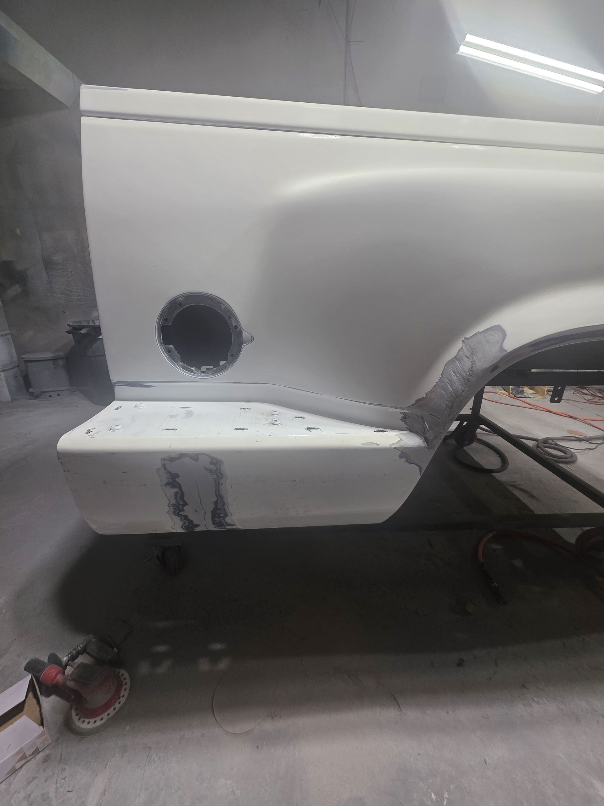 White car body panel in a repair shop with a round cutout and visible sanding/primer marks.