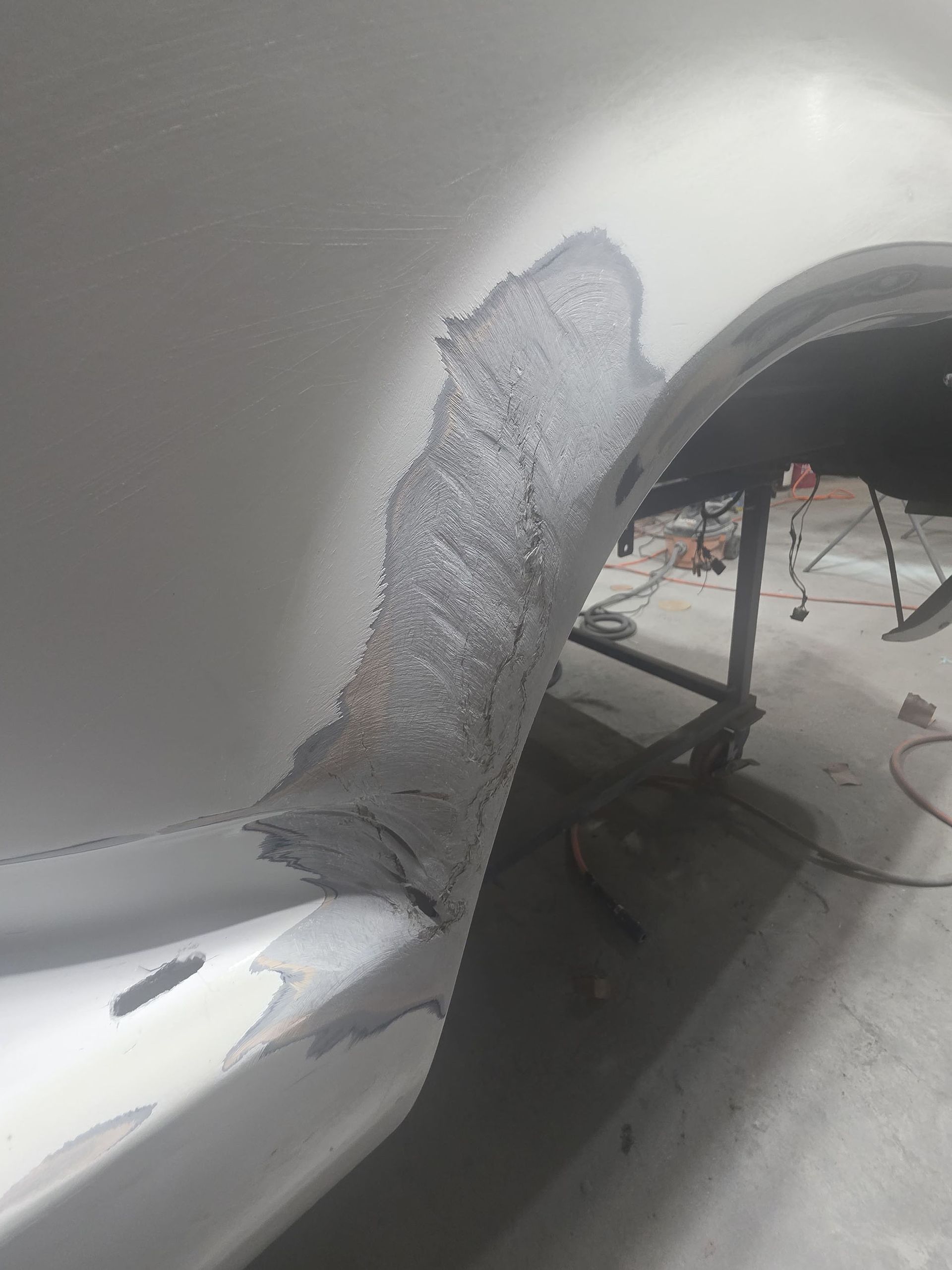 Close-up of a gray car’s damaged wheel arch with peeling paint and a dent near the tire opening
