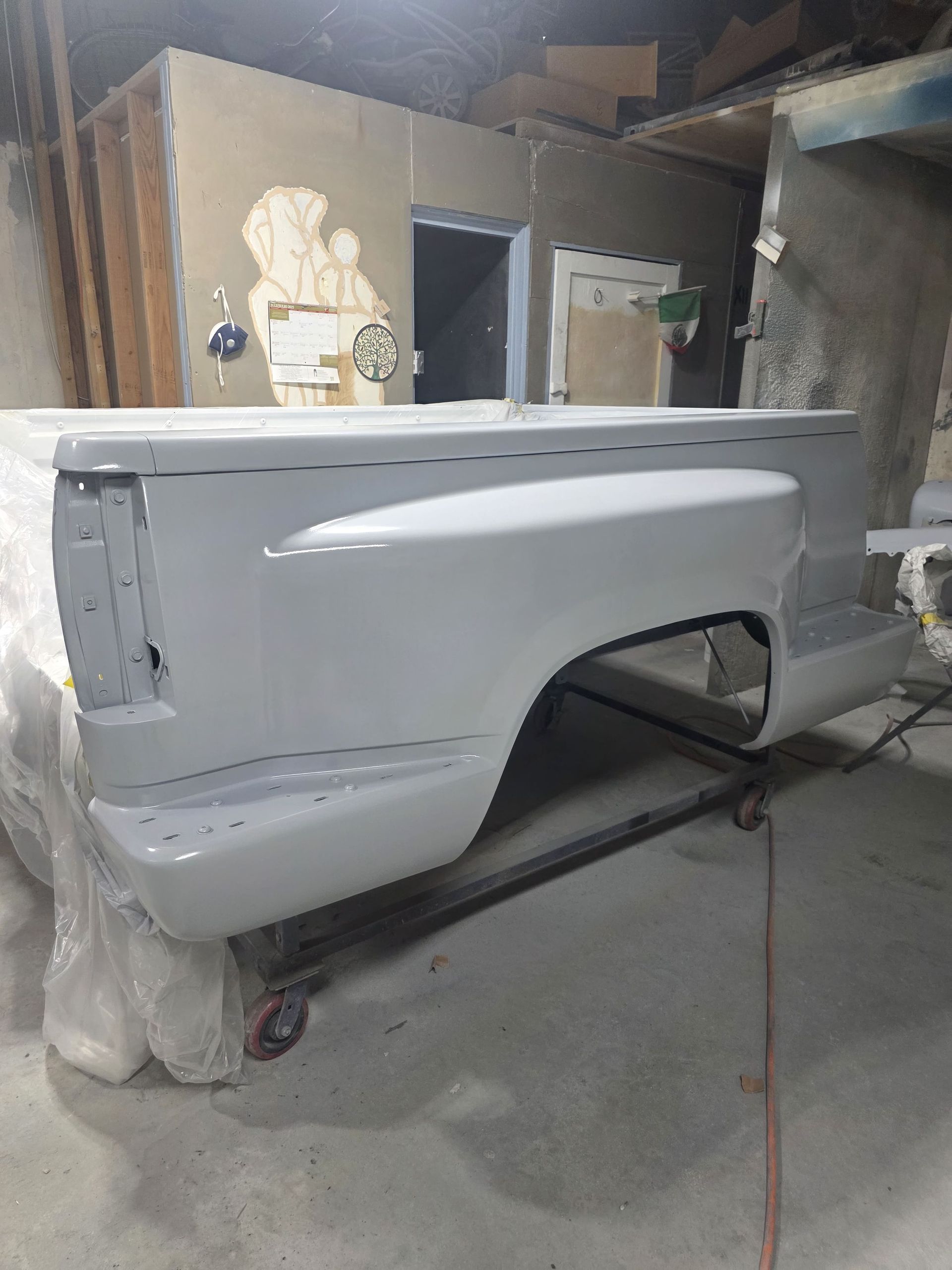 Primed white pickup truck bed in an auto body shop, mounted on a rolling dolly.