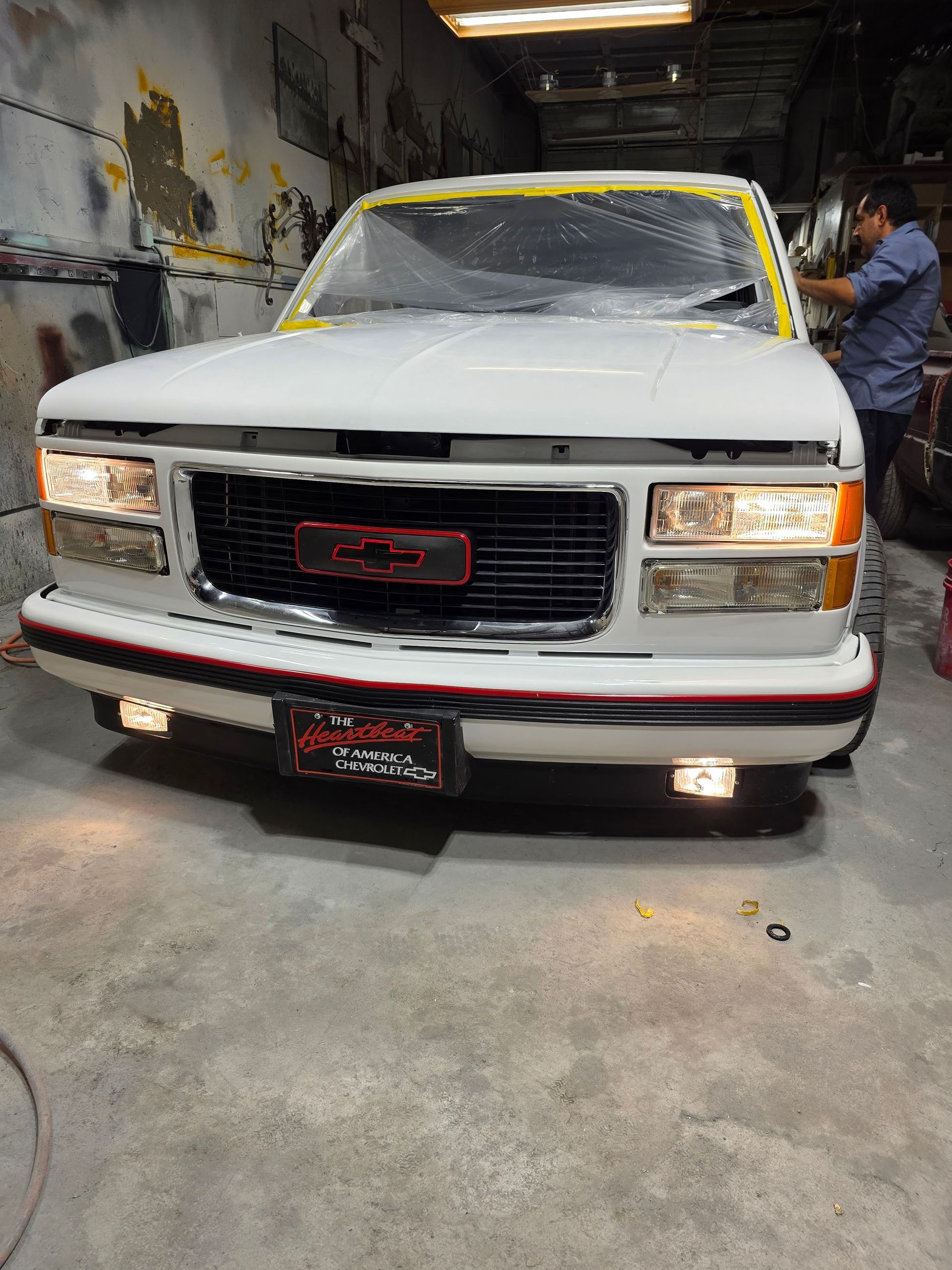 White classic pickup truck in a garage, front view, with a person working beside it