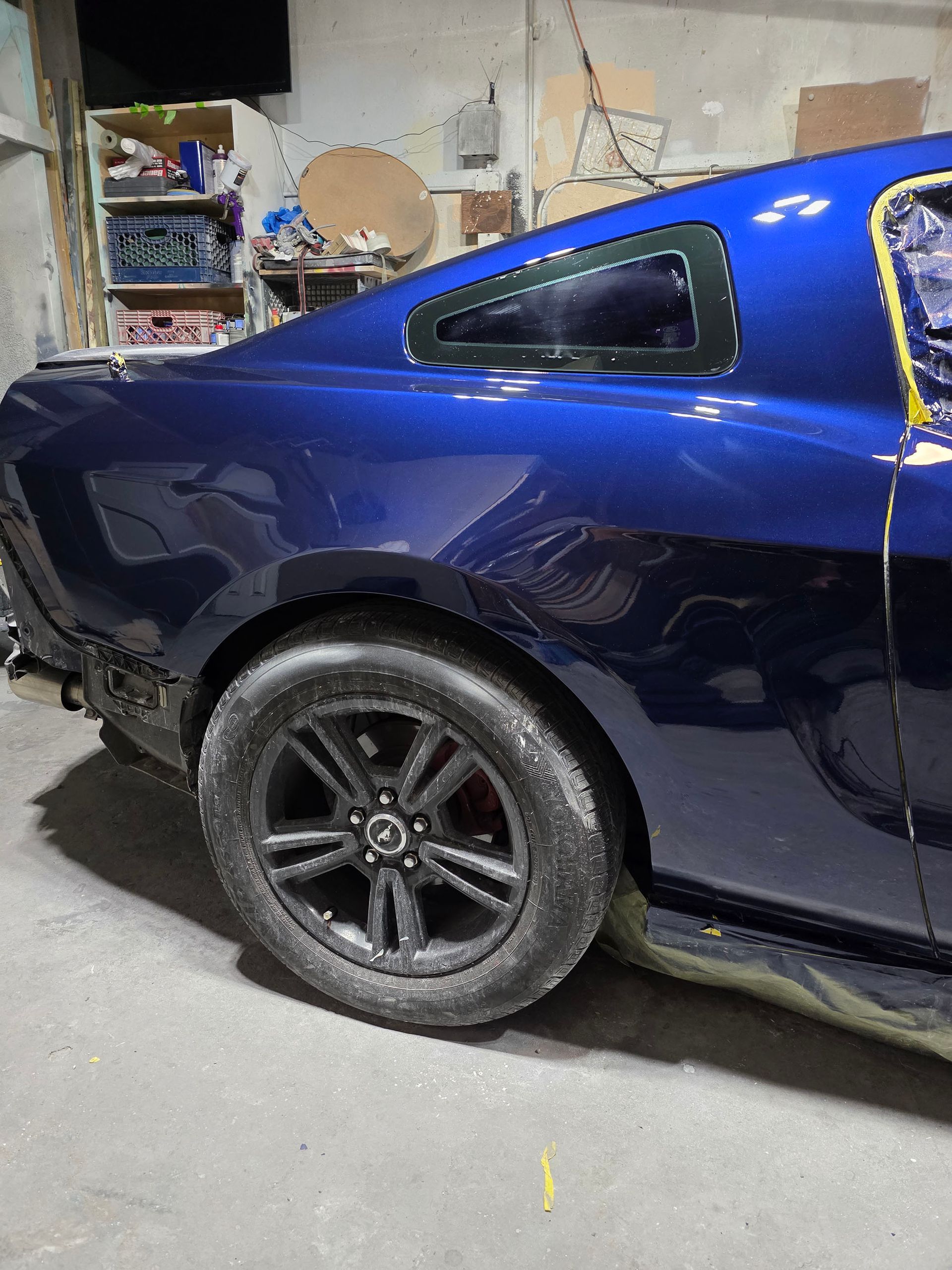 Blue sports coupe in a garage with a black rear wheel and a masked rear side window area
