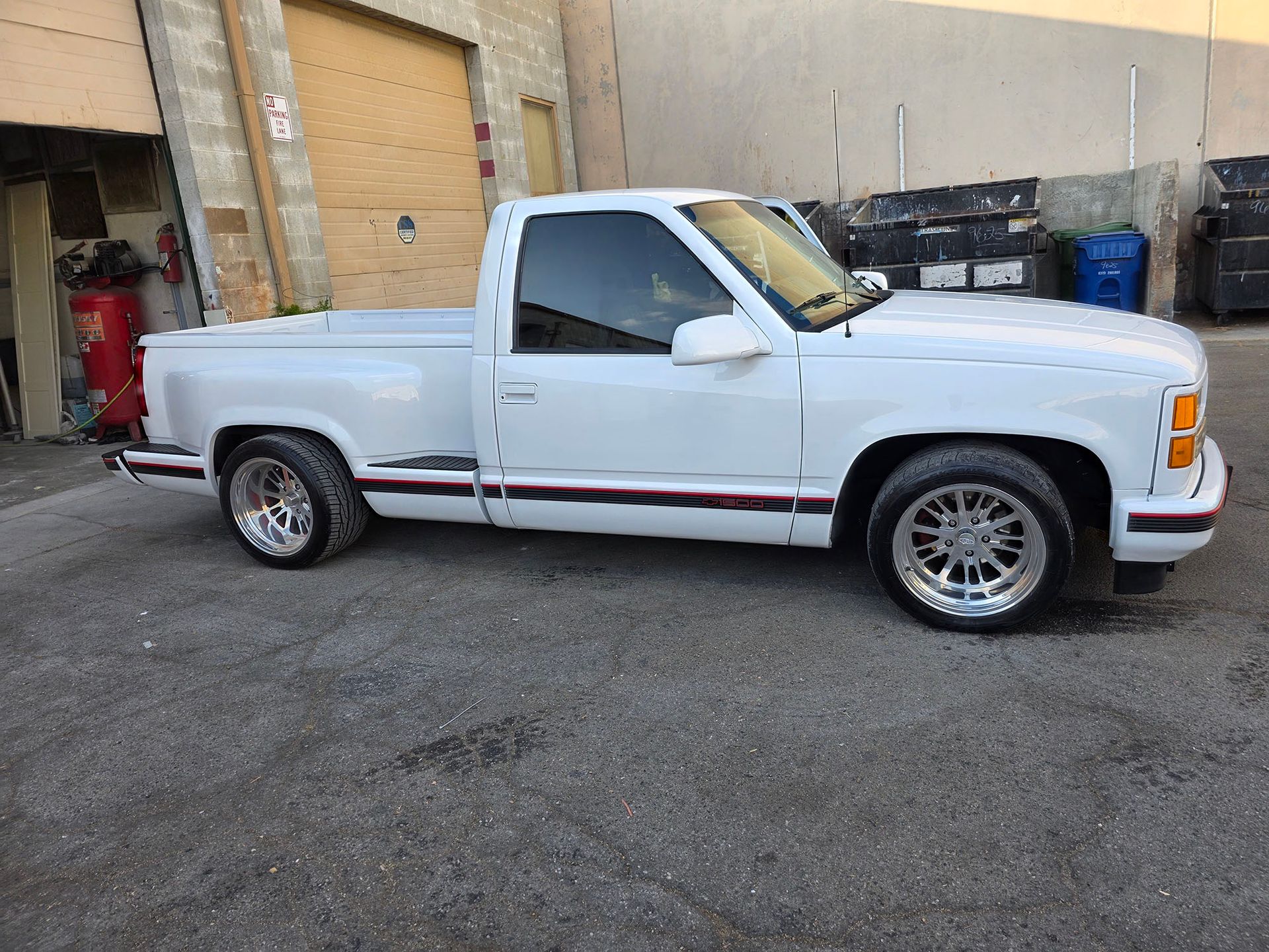 White pickup truck parked beside a brick building in an industrial lot
