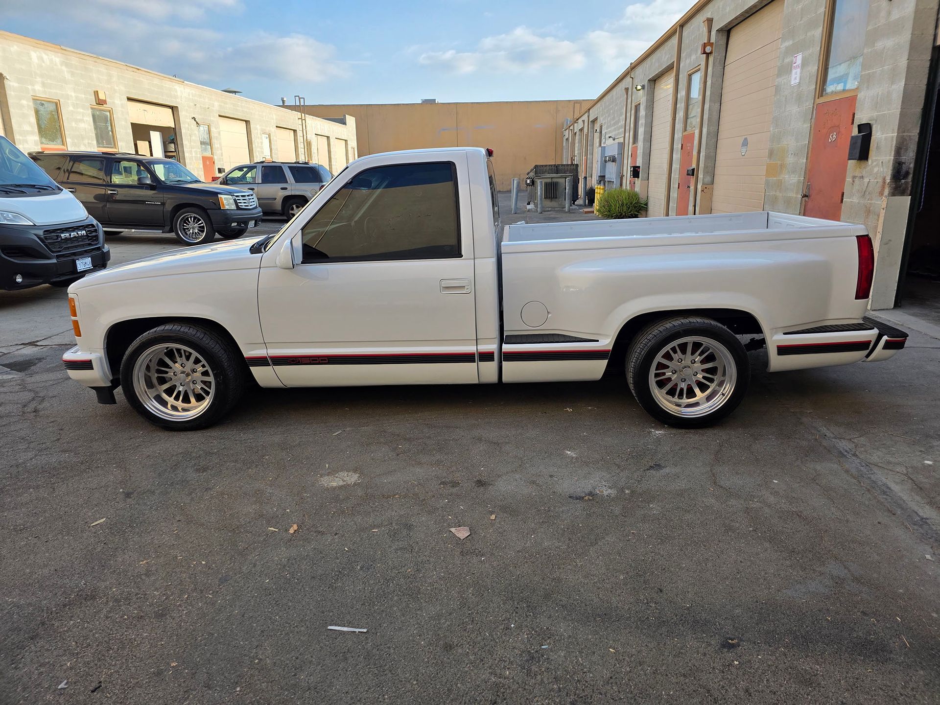 White single-cab pickup truck parked in an industrial lot beside beige buildings