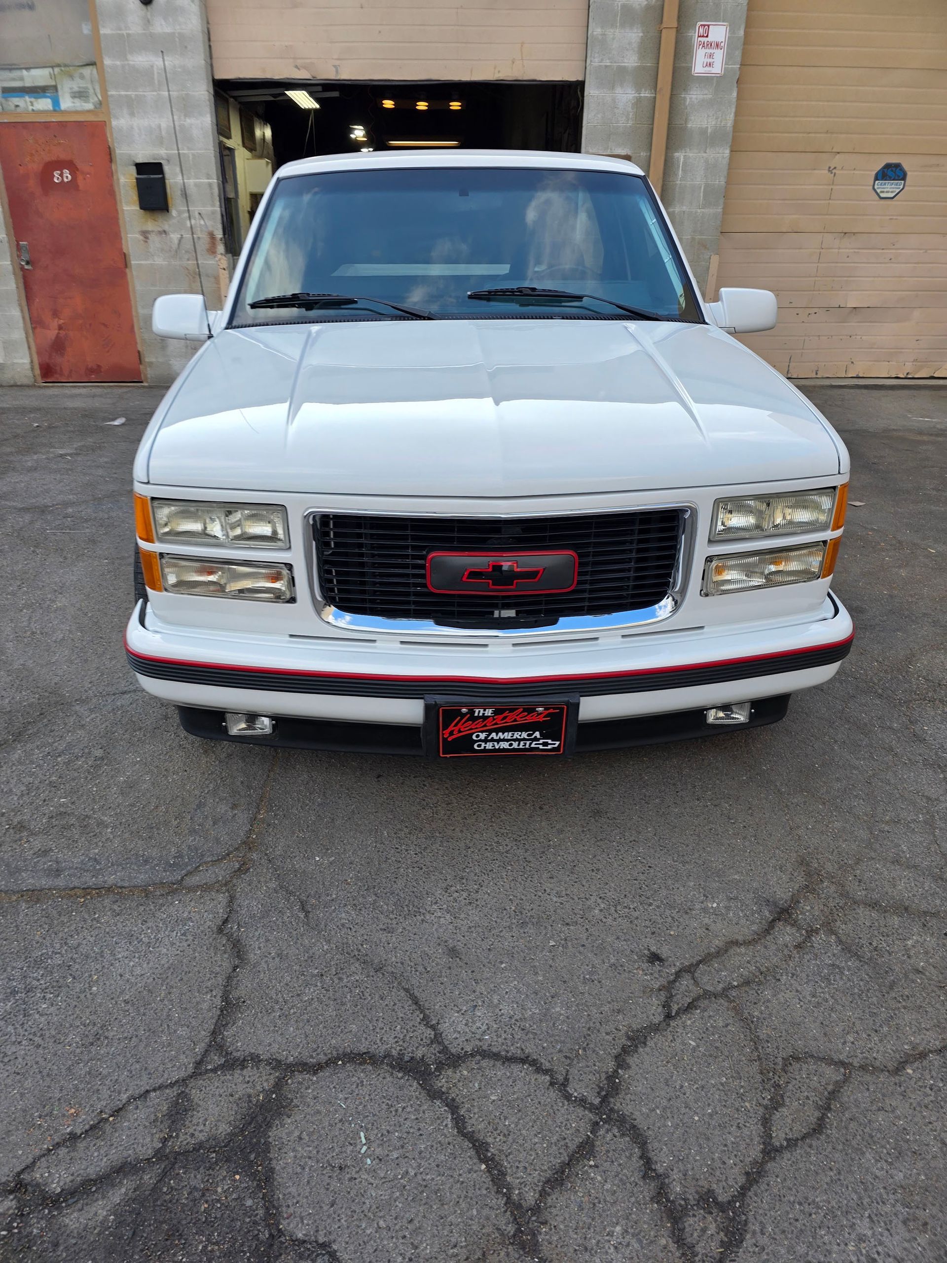 White GMC truck parked in front of a garage, facing the camera.