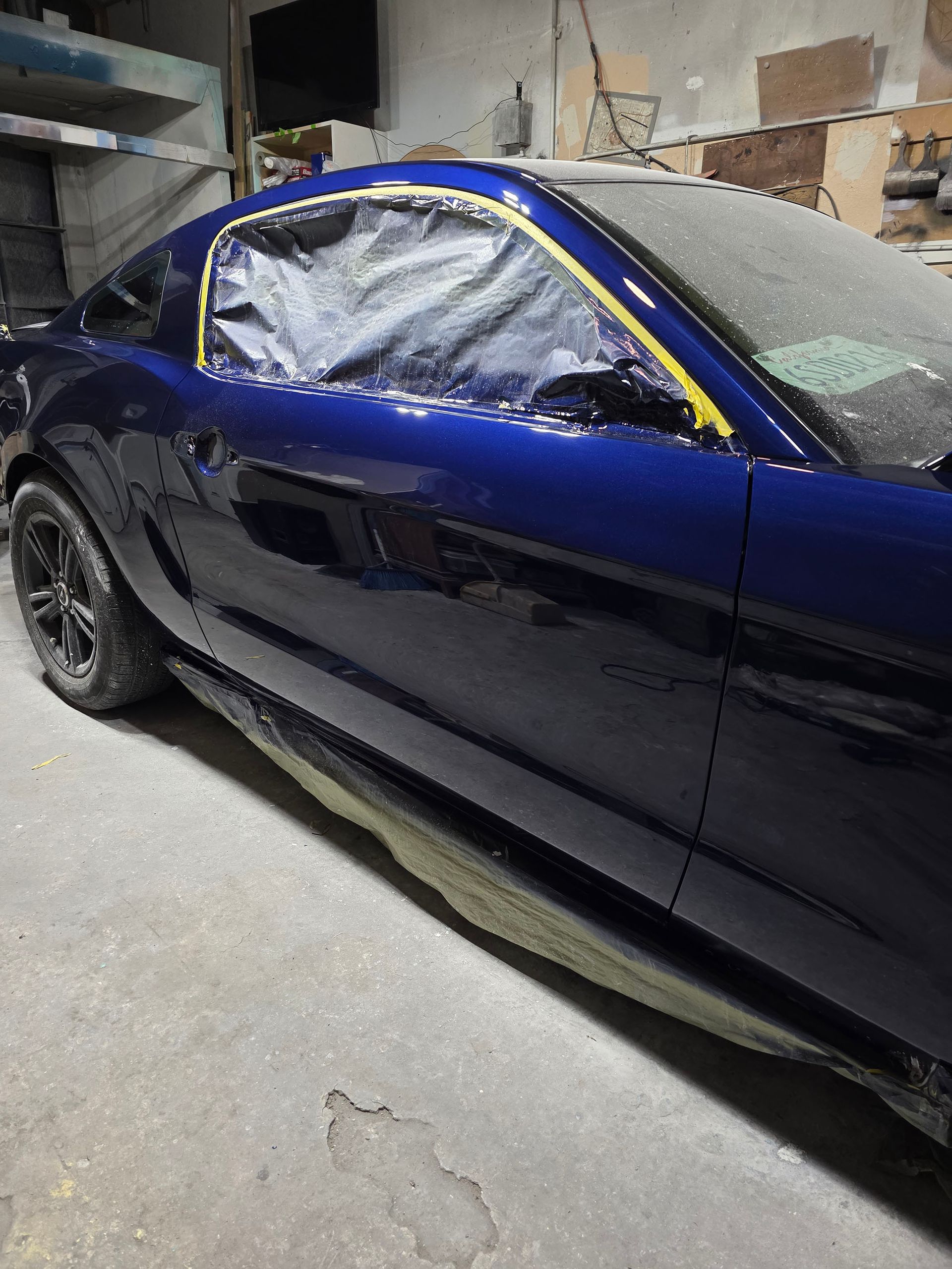 Blue sports car with taped windows parked inside a workshop, partially covered in dust.