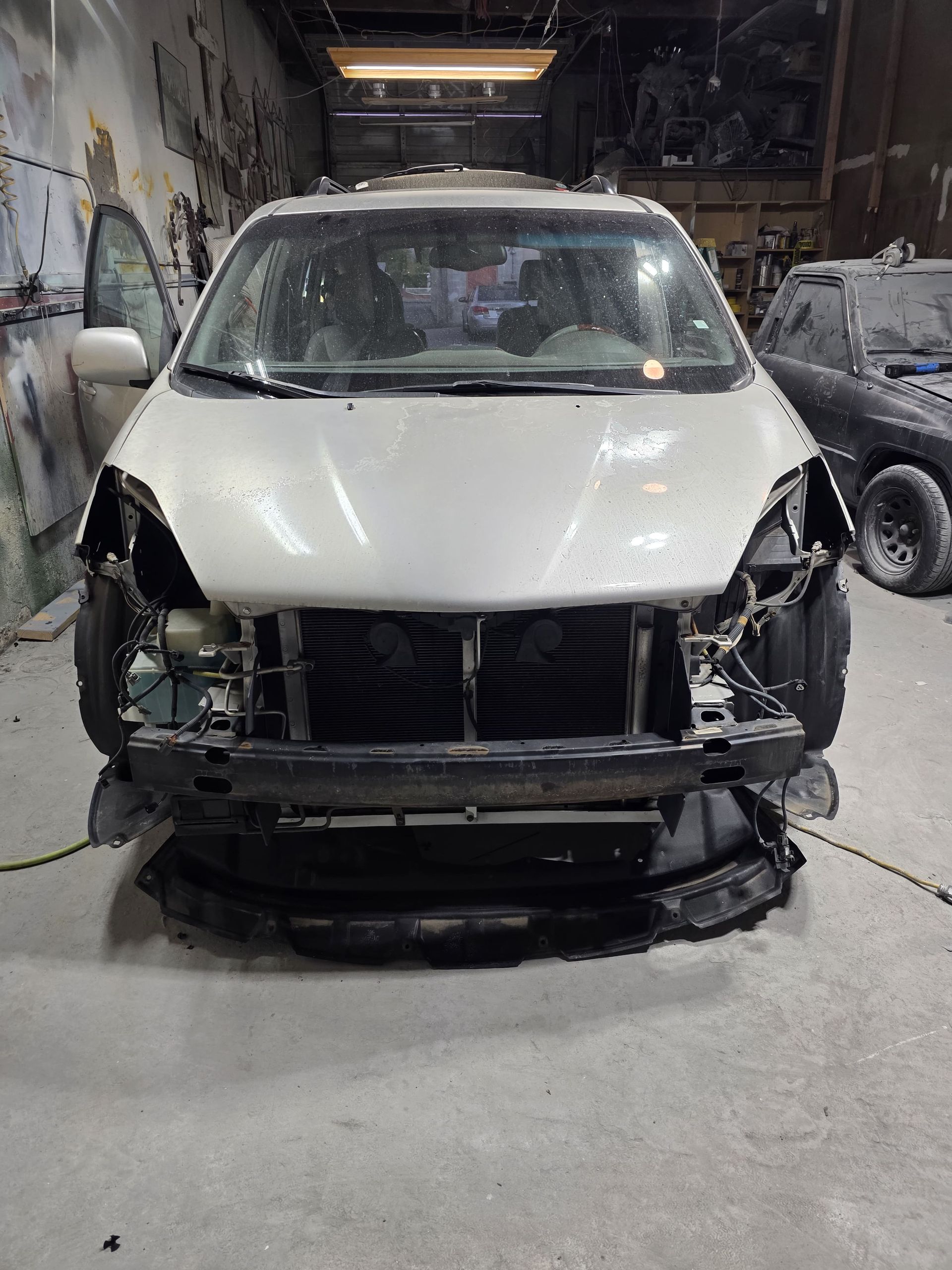 Damaged white SUV with missing front bumper and exposed front end in a garage