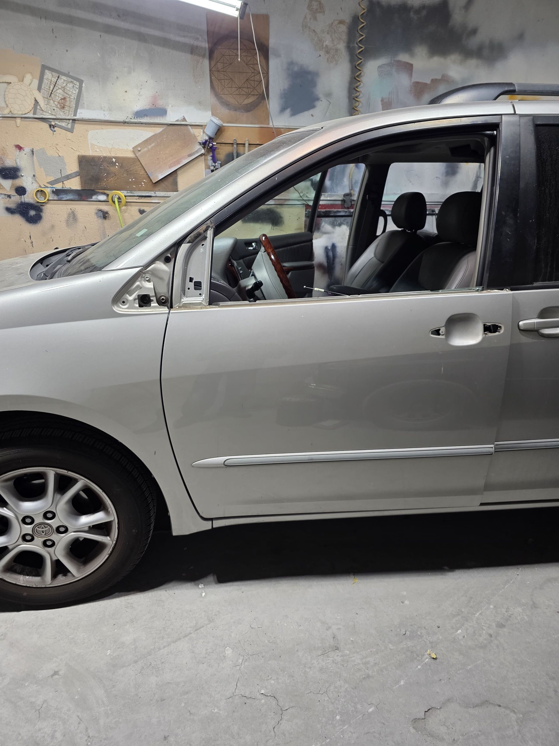 Silver sedan parked in a garage, with the driver-side window broken out.