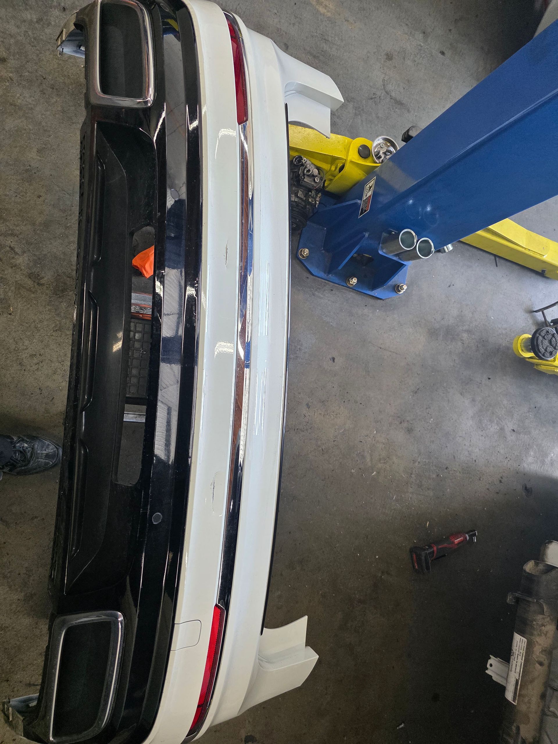 White car in a workshop, seen from above beside a blue lift and yellow jack stands.