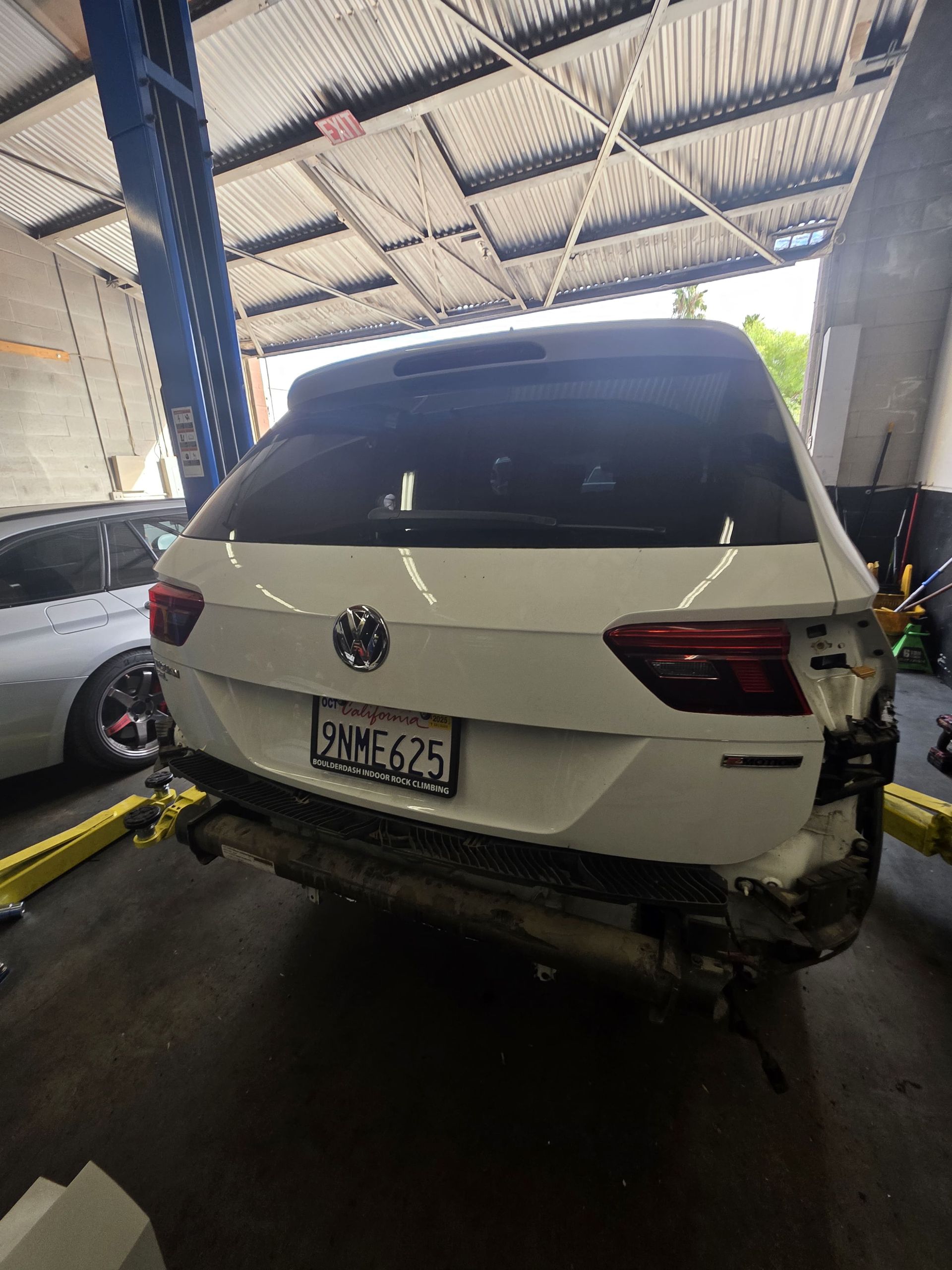 White Volkswagen SUV on a lift in an auto repair shop, rear view under a metal roof