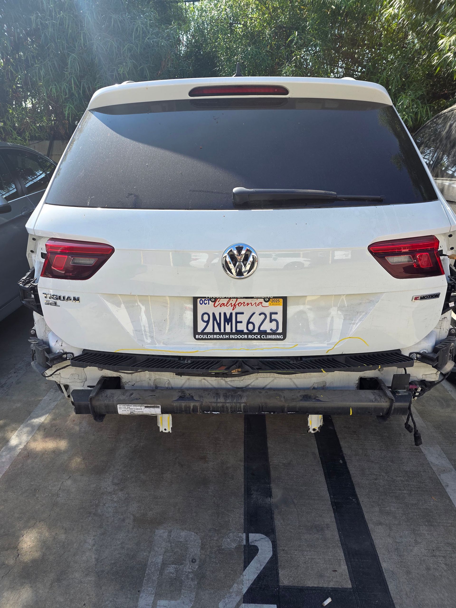 Rear view of a white Volkswagen SUV with rear-end crash damage and a visible license plate.