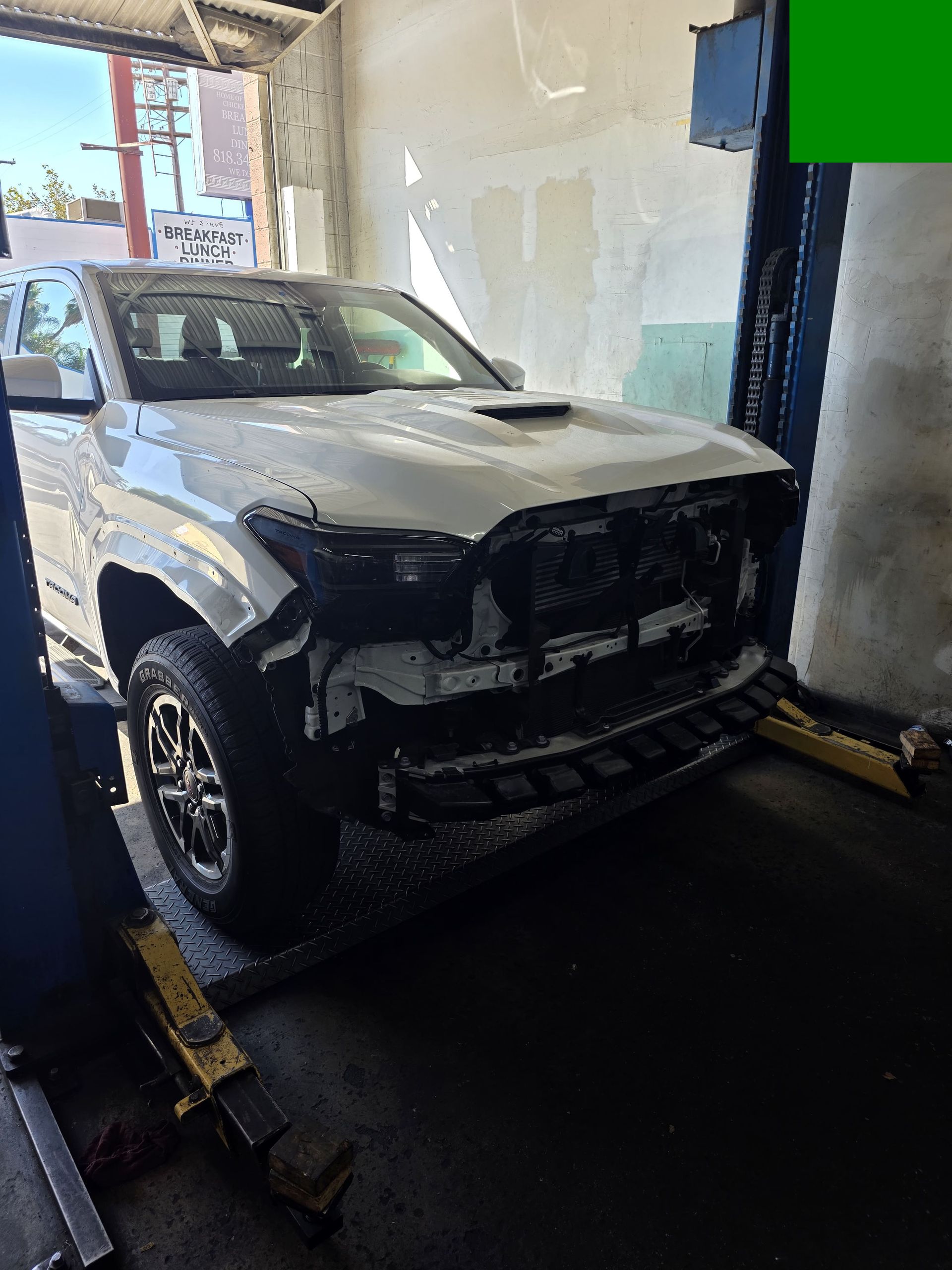 White pickup truck inside a garage, front end heavily damaged and missing the grille.